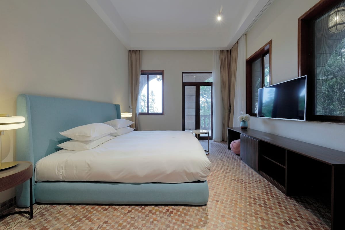 A hotel room with a bed, a TV, a lamp, and a window with curtains.