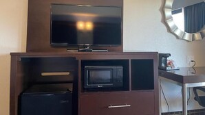 Une chambre d’hôtel équipée d’un téléviseur à écran plat posé sur un meuble en bois, d’un four à micro-ondes, d’un petit réfrigérateur et d’un miroir rond fixé au mur.