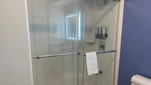 Une cabine de douche fermée par des parois en verre, équipée d’un porte-serviettes et d’un distributeur de savon, et dont on aperçoit les toilettes dans la pièce adjacente.
