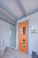 Et værelse med dør i træ, et hvidt toilet og en brusekabine i glas.