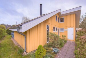 En gul bygning med skråt tag, skorsten og en lille have.