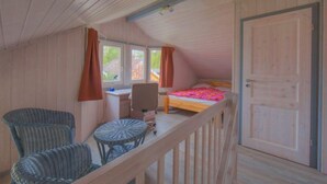 A cozy attic bedroom with a wooden ceiling, a bed with a colorful bedspread, a desk with a chair, and a small round table. - Ferienhaus im Ferienpark Mirow (Mirow)
