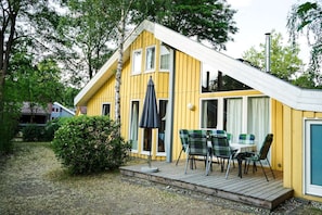 Ein gelbes Haus mit geneigtem Dach, einer Terrasse mit Tisch und Stühlen und einem großen Sonnenschirm.