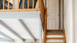 Una escalera de madera con una cesta al pie, un comedor con sillas y mesa de madera, y una cocina con armarios de madera.