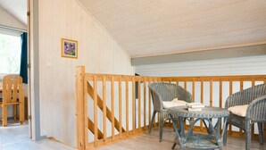 Una habitación con piso de madera, baranda de madera, sillas de mimbre y una pequeña mesa.