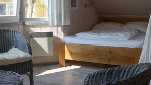 Un dormitorio acogedor en el ático con una cama de madera, dos sillones de mimbre, una mesita y una ventana con cortinas.