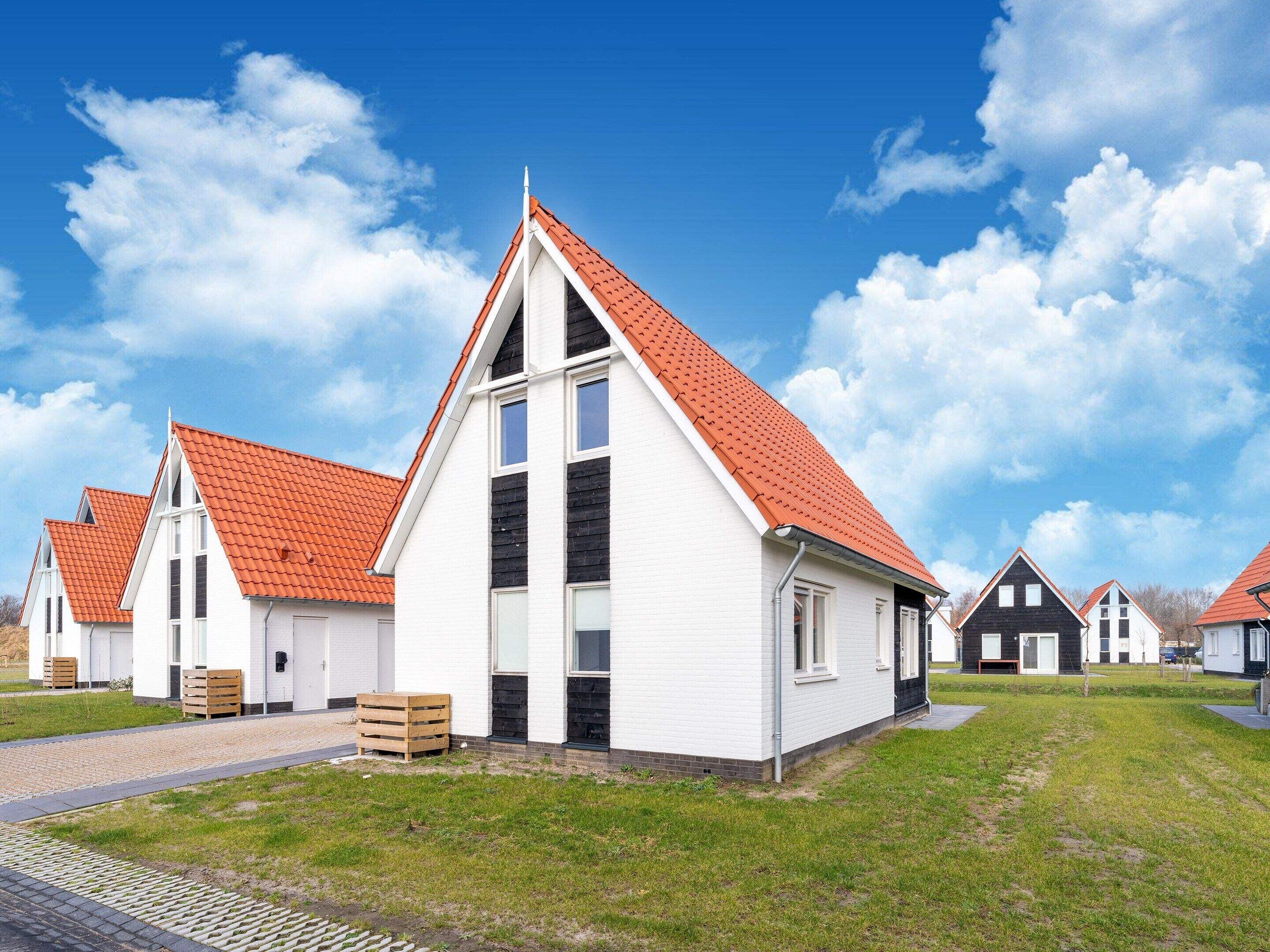 A row of white houses with red roofs and black accents, arranged in a row on a grassy area with a clear blue sky.