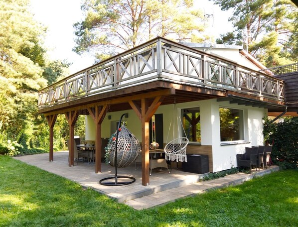 A covered outdoor seating area with a wooden deck, hanging chairs, and a hanging light fixture. - Holiday Home on the Lake Shore, Sauna, Jacuzzi (gmina Stężyca)