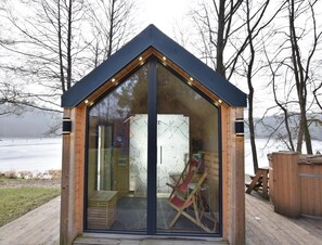 Uma cabana de madeira com paredes de vidro, teto inclinado, deck de madeira e vista para um lago.