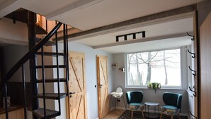 A modern interior with a spiral staircase, wooden doors, two chairs, a small table, and a window with a view of trees.