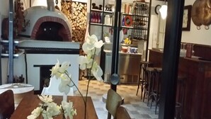 Un comedor con una mesa y sillas de madera, un jarrón con flores blancas y un horno de ladrillo al fondo.