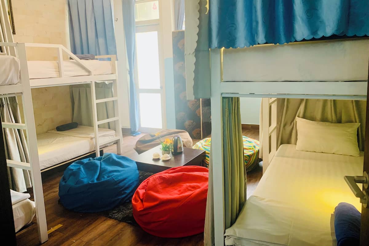 A dormitory room with bunk beds, a small table with a vase of flowers, and bean bags.