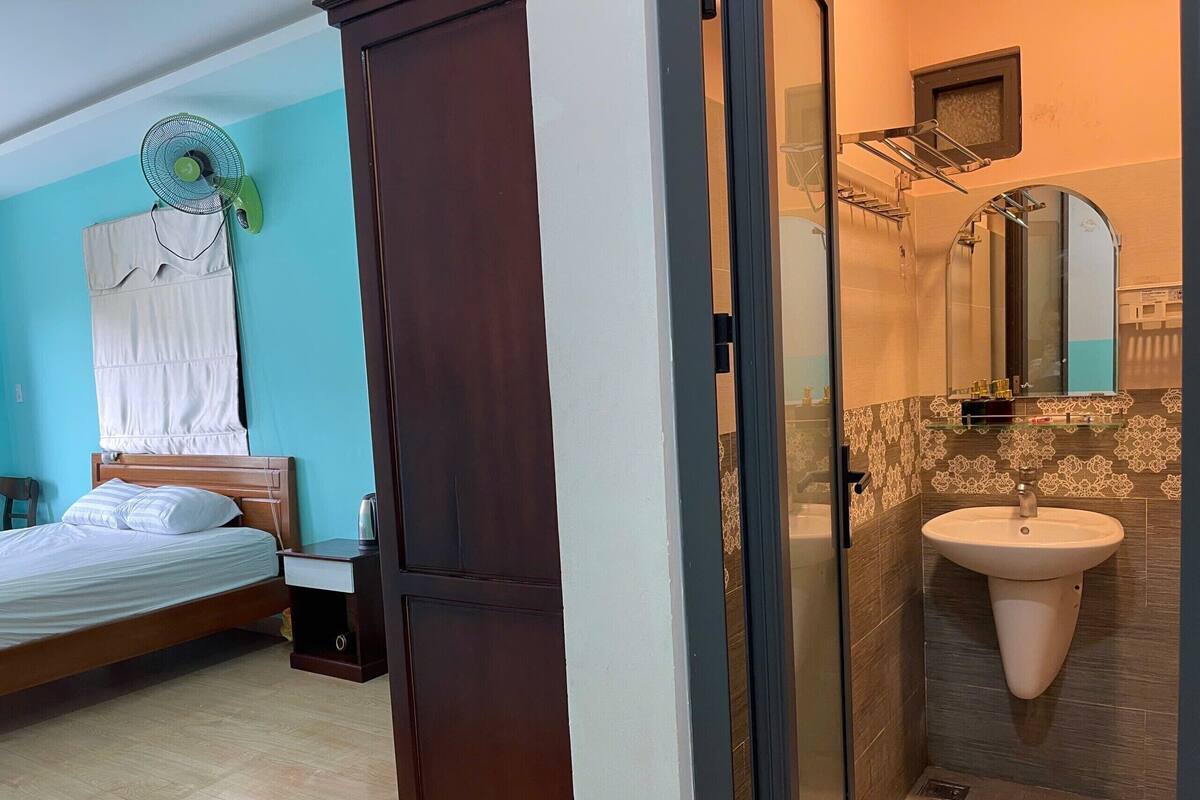 A bedroom with a bed, a bedside table, and a wall-mounted fan.