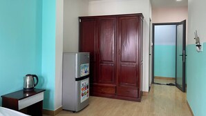 A compact room with teal walls, a wooden wardrobe, a refrigerator, and a small table with a kettle. - Bunk Beach Hostel (Da Nang)