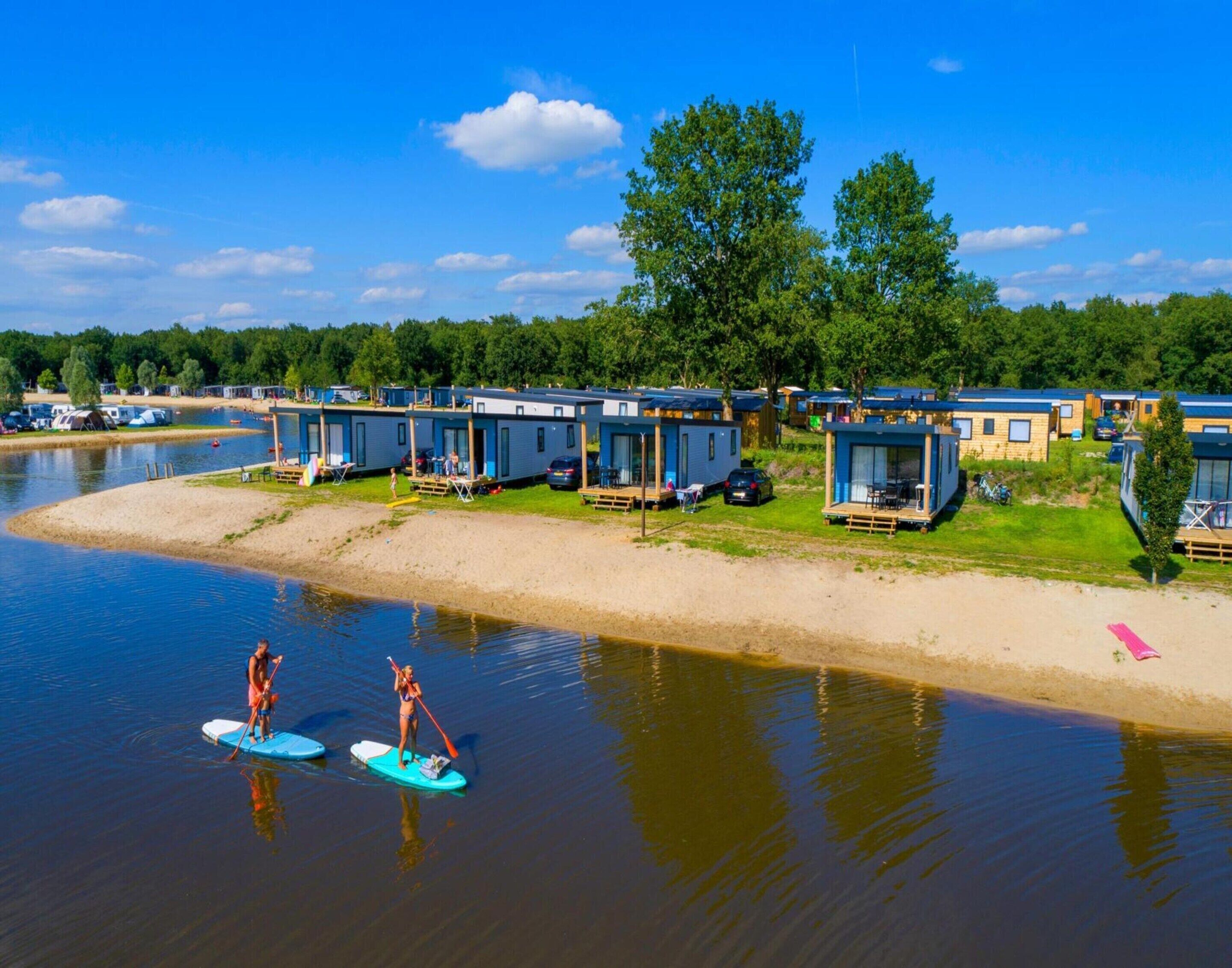 A lakeside camp with floating cabins and paddleboarders on the water.