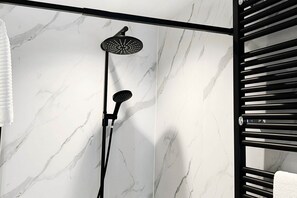 Un baño moderno con pared de mármol, cabezal de ducha negro y un perchero.