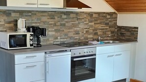A modern kitchen with white cabinets, a stone backsplash, a built-in oven, and a coffee maker. - Apartment 50 sqm with separate bedroom and balcony (Aschau im Chiemgau)