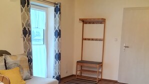 A room with a wooden floor, a sofa with cushions, a wooden chair, a coat rack, and a door. - Apartment 50 sqm with separate bedroom and balcony (Aschau im Chiemgau)