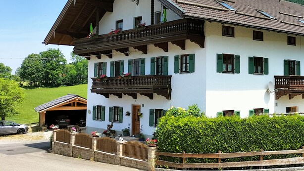 A traditional chalet with a sloped roof, wooden balconies, and green shutters. - Apartment 50 sqm with separate bedroom and balcony (Aschau im Chiemgau)