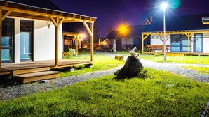 Een goed verlichte buitenruimte met een houten terras, een overdekte zithoek en een gebouw met een nummerbord '6'.