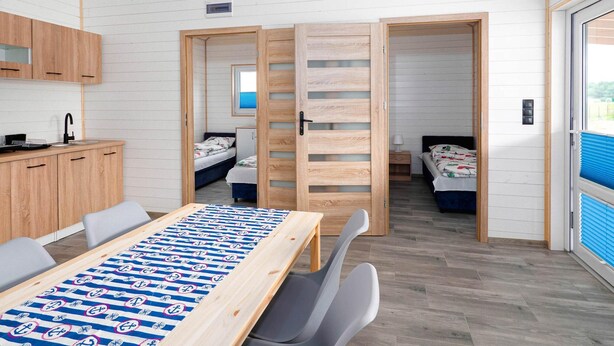 Een moderne, compacte kamer met een houten tafel, twee bedden, een kitchenette en een groot raam.