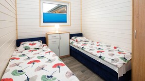 Een compacte kamer met twee eenpersoonsbedden, een klein bureau en een raam met uitzicht op een gebouw.