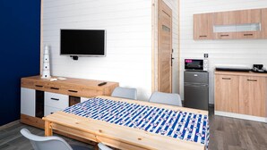 Een compacte kamer met een bed, een bureau, een televisie, een magnetron en een kleine kitchenette.