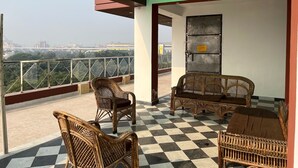 Ein Balkon mit Korbmöbeln, einem Schachbrettfußboden und Blick auf die Stadt.