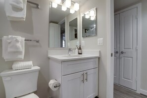 Une salle de bain avec des toilettes blanches, un lavabo avec un miroir au-dessus et un porte-serviettes.