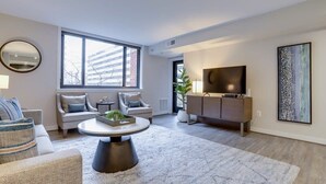 Una sala de estar moderna con un conjunto de sofás, una mesa de centro, un televisor y un ventanal grande.