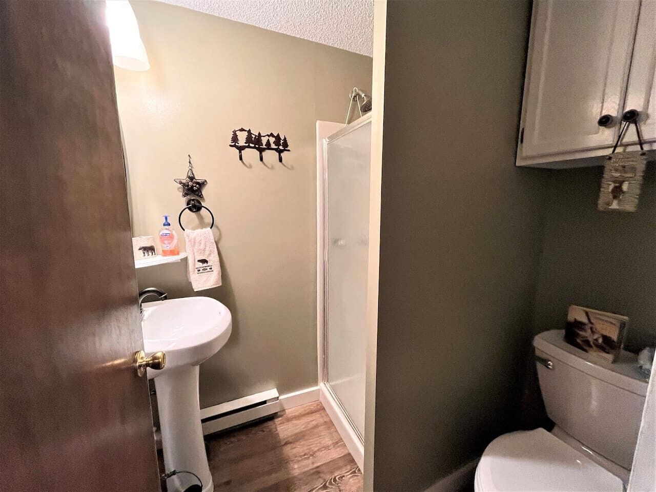 Een badkamer met een witte wastafel, een toilet en een douche. Er hangt een handdoek aan de muur en er is een klein plankje met toiletartikelen.