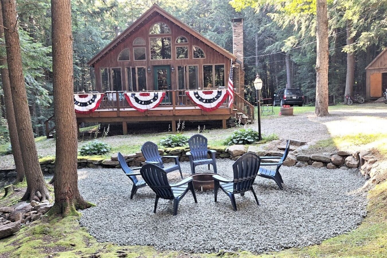 A wooden cabin with a deck, surrounded by trees and gravel.