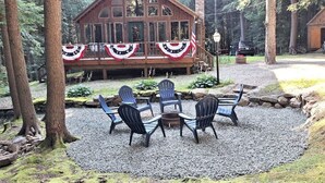 Une cabane en bois dotée d’une terrasse, entourée d’arbres et de gravier.