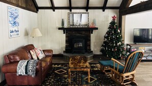 Un salon chaleureux avec une cheminée, un sapin de Noël, un canapé en cuir et un téléviseur.