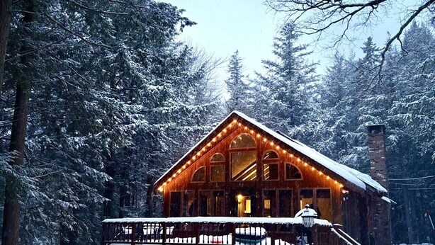 Une cabane en bois dotée d’une terrasse couverte et surplombant un paysage enneigé.