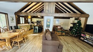 Un intérieur rustique avec une table à manger en bois, un canapé marron, un coin cuisine et un sapin de Noël.