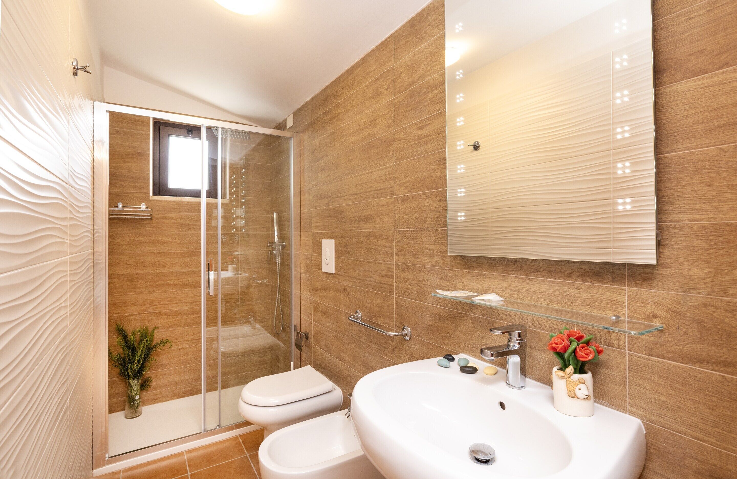 A modern bathroom with a glass shower enclosure, a white sink, and a mirror above it.