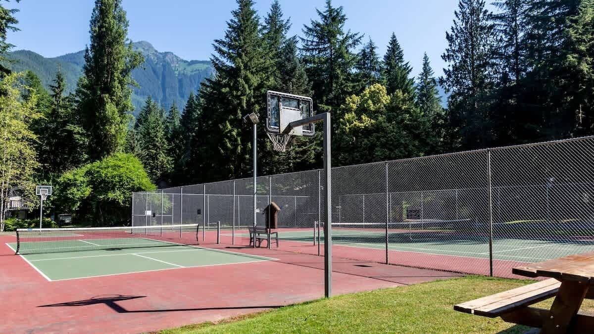 Ein Tennisplatz im Freien mit Netz, umzäunt und mit einem Picknicktisch im Vordergrund.