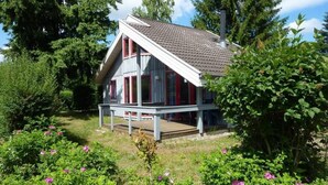 A house with a sloped roof, a porch, and a garden with pink flowers. - Exklusives Skandinavisches Ferienhaus (Mirow)