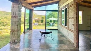 A covered patio area with a view of a grassy landscape, a brick pillar, and a glass door leading outside.