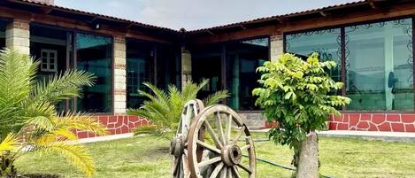 A building with a courtyard, featuring a large wooden wheel, palm trees, and a brick facade.