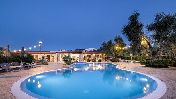 A swimming pool with lounge chairs and umbrellas, surrounded by trees and a building with a red roof. - Farmhouse in Vieste Near Gargano Coast (Vieste)