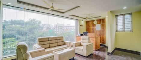 A modern hotel lobby with a sofa set, a wooden reception desk, and large windows offering a view of the cityscape.