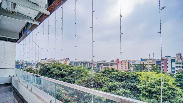 Un balcon doté d’une balustrade en verre, offrant une vue sur un paysage urbain avec des bâtiments et de la verdure.