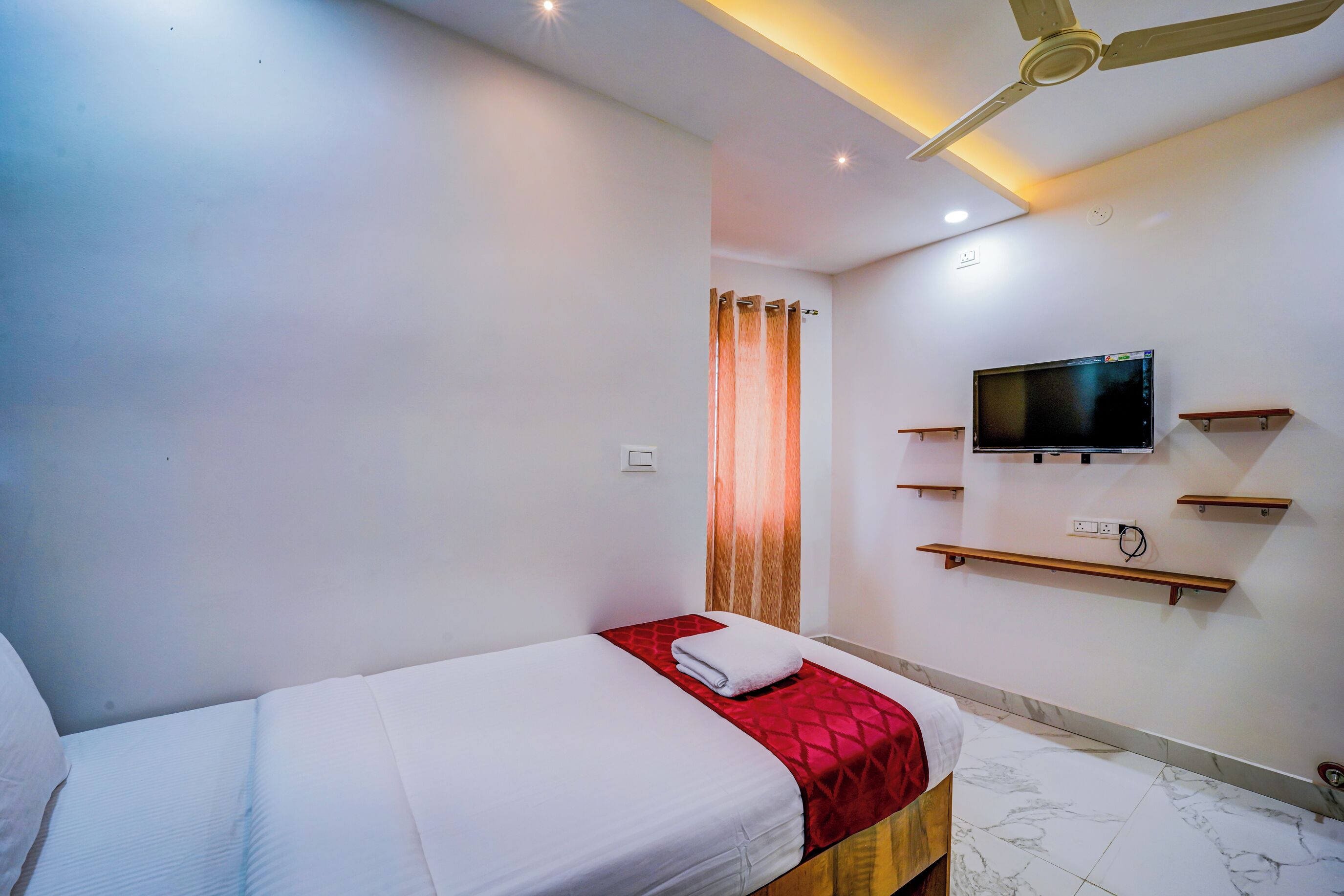 A hotel room with a bed, a TV mounted on the wall, and a ceiling fan.