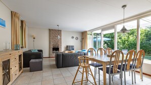 Een ruime woonkamer met een eettafel, stoelen, een bank en een open haard.
