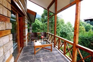 A wooden balcony with stone walls, two chairs, and a glass table. - Banon Resorts (Manali)