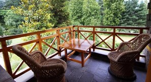 Ein Balkon mit Korbmöbeln, einem Tisch und Blick auf einen üppigen Garten.