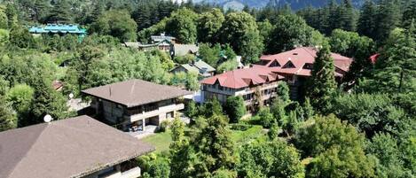 A mountain resort with multiple buildings surrounded by dense forest and snow-capped peaks in the background.