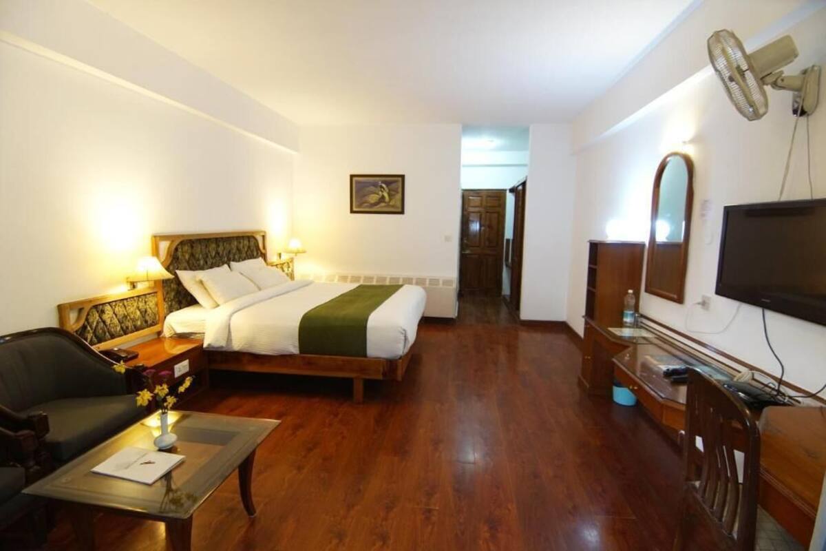 A hotel room with a bed, a desk, a chair, a television, and a fan.